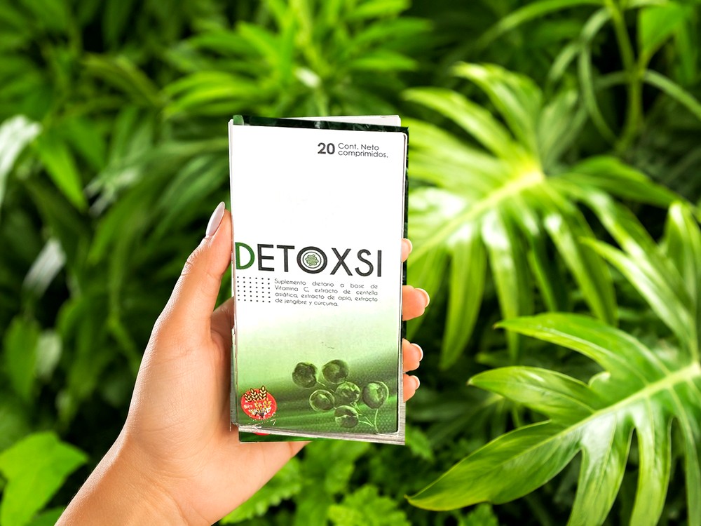 Mano sosteniendo la caja de DetoxSi entre hojas verdes